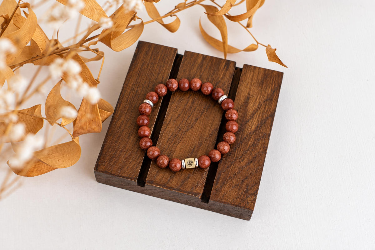 A bracelet with reddish-brown round beads and silver-toned spacers rests on a dark wooden surface.