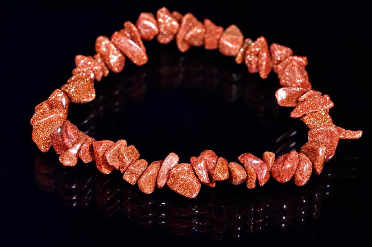 A bracelet made of irregular, reddish-brown goldstone chips with a glittering texture, arranged in a circle on a dark reflective surface.