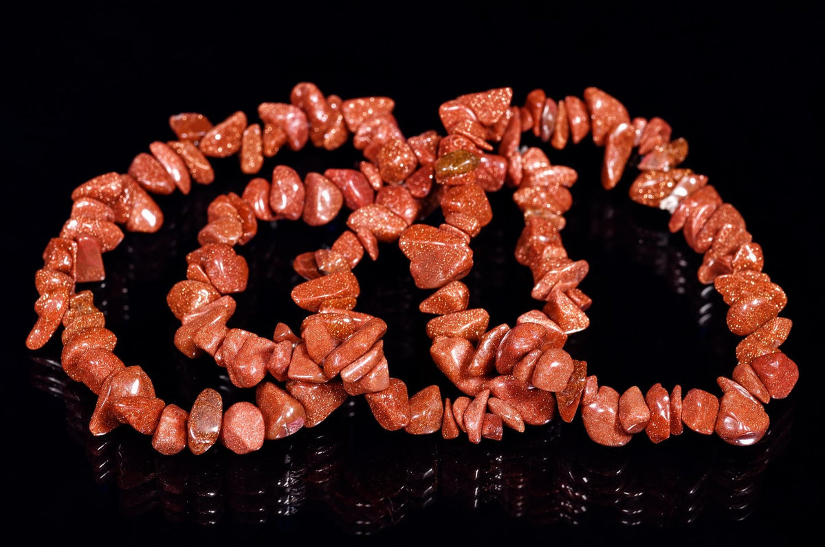 A bracelet made of reddish-brown, glittering chip-shaped beads arranged in a loose coil on a dark, reflective surface.