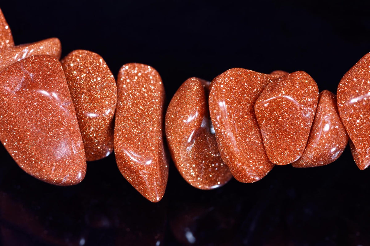 A string of polished, reddish-brown goldstone chips with a glittering texture arranged on a dark surface.