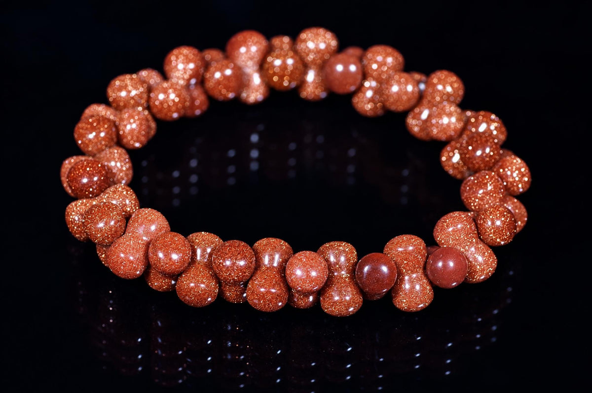 A bracelet made of round, reddish-brown beads with a glittery goldstone finish, arranged in a circle on a dark reflective surface.