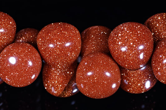 Close-up of a goldstone bracelet showing reddish-brown sparkling beads with rounded, curved shapes against a dark background.