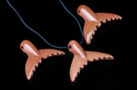 Three goldstone dolphin-tail pendants on a blue cord, resting on a dark reflective surface.
