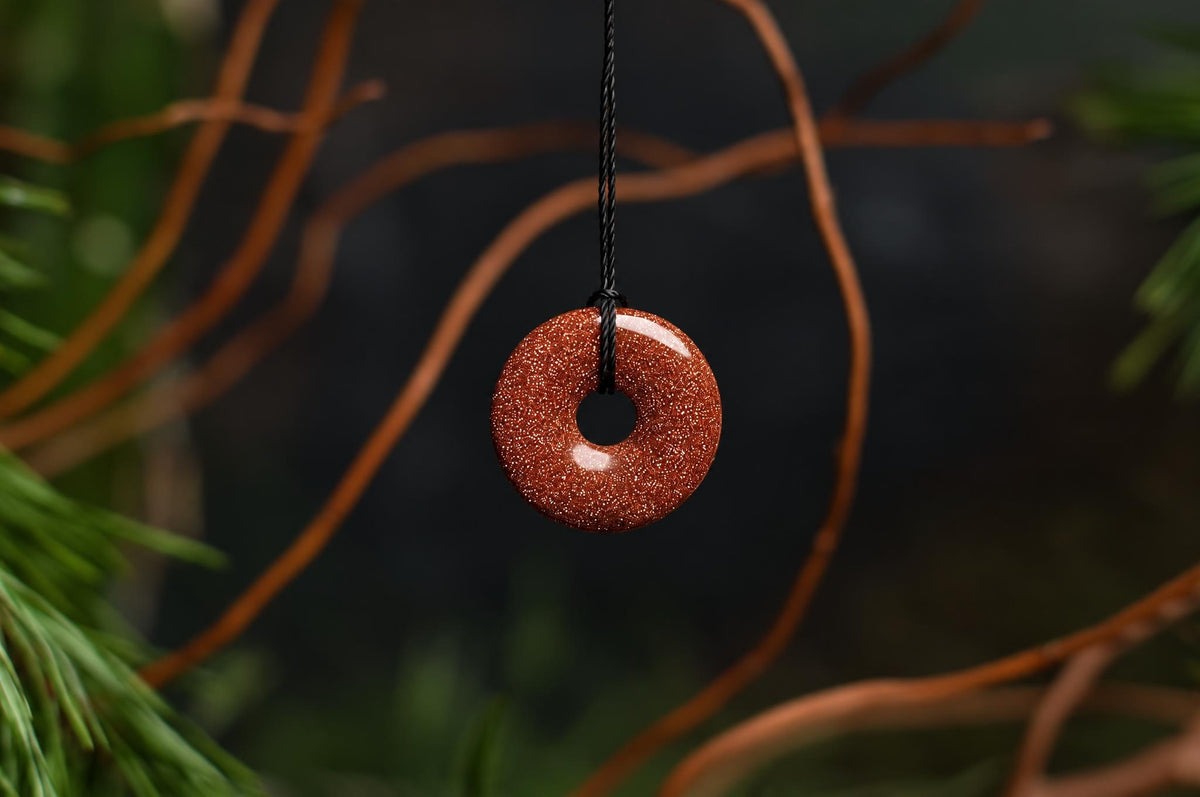 A donut-shaped pendant with a sparkly reddish-brown surface hangs from a black cord against a dark background.