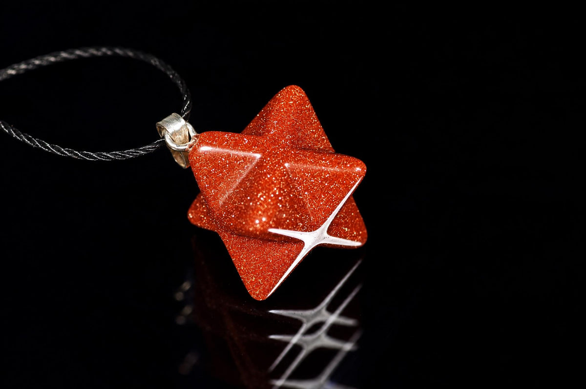 A red, glittery star-shaped pendant on a dark cord against a black background.