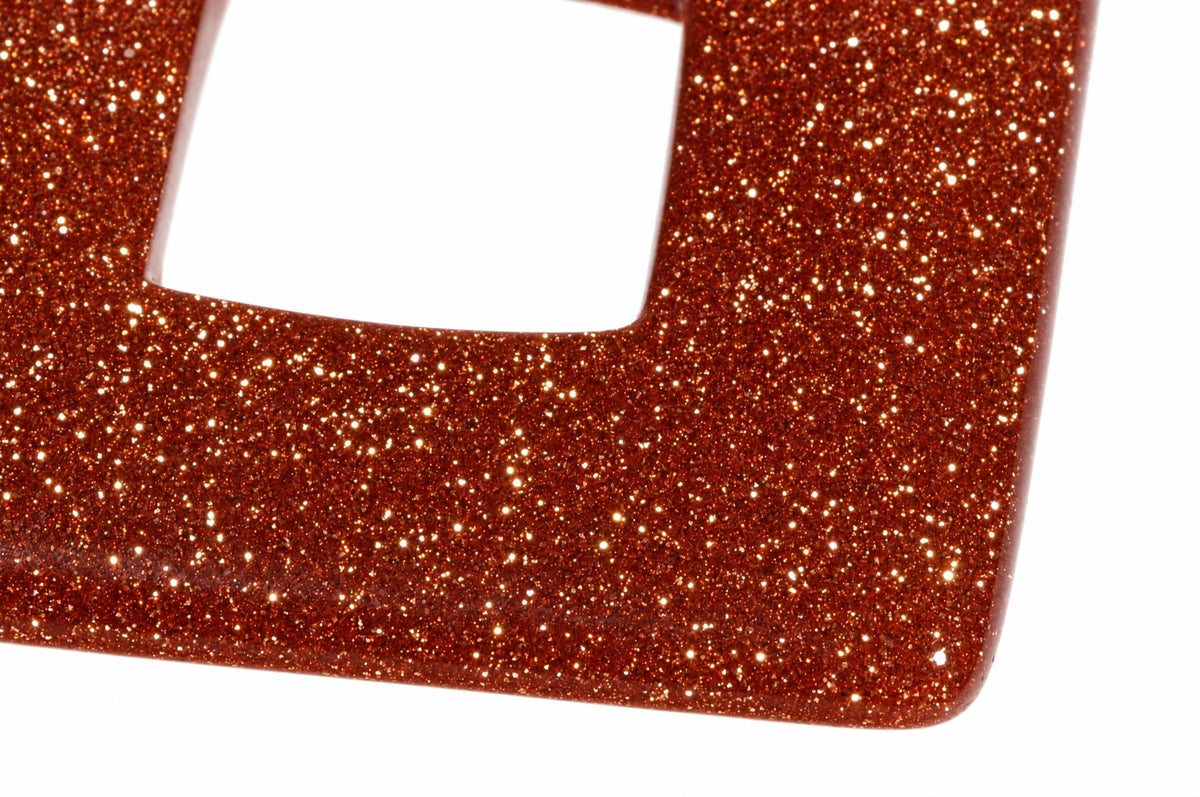 Close-up of a reddish-brown square goldstone pendant with sparkling flecks and a central square opening against white.