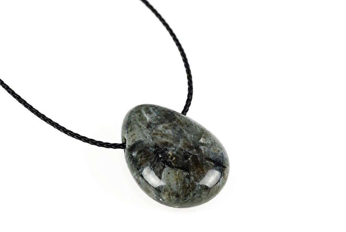 A rounded gray pendant shows irregular black and pale mottling beneath its glossy surface, suspended from a black cord against white.