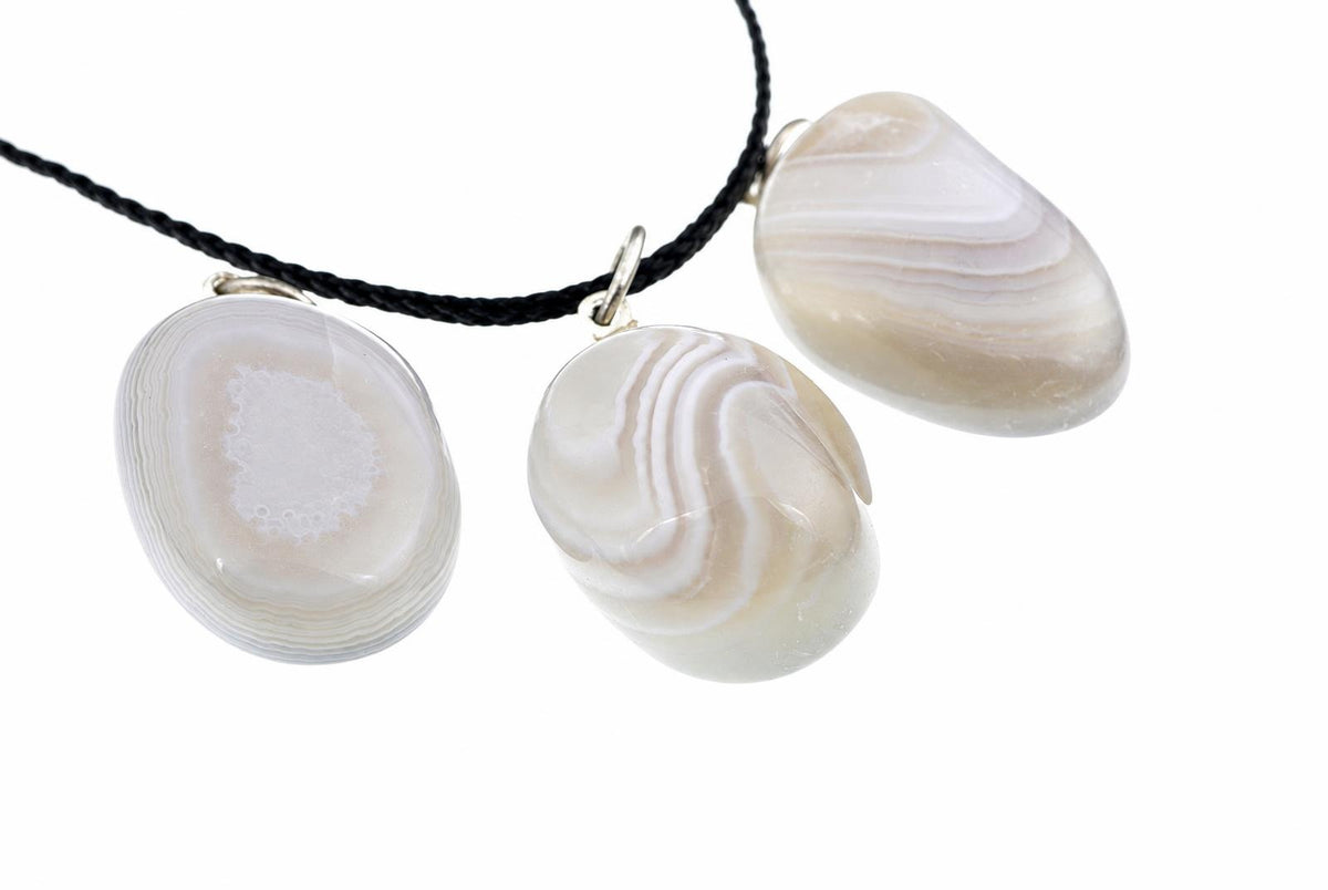 Three polished agate pendants with white and grey banding hang from a black cord against a white background.