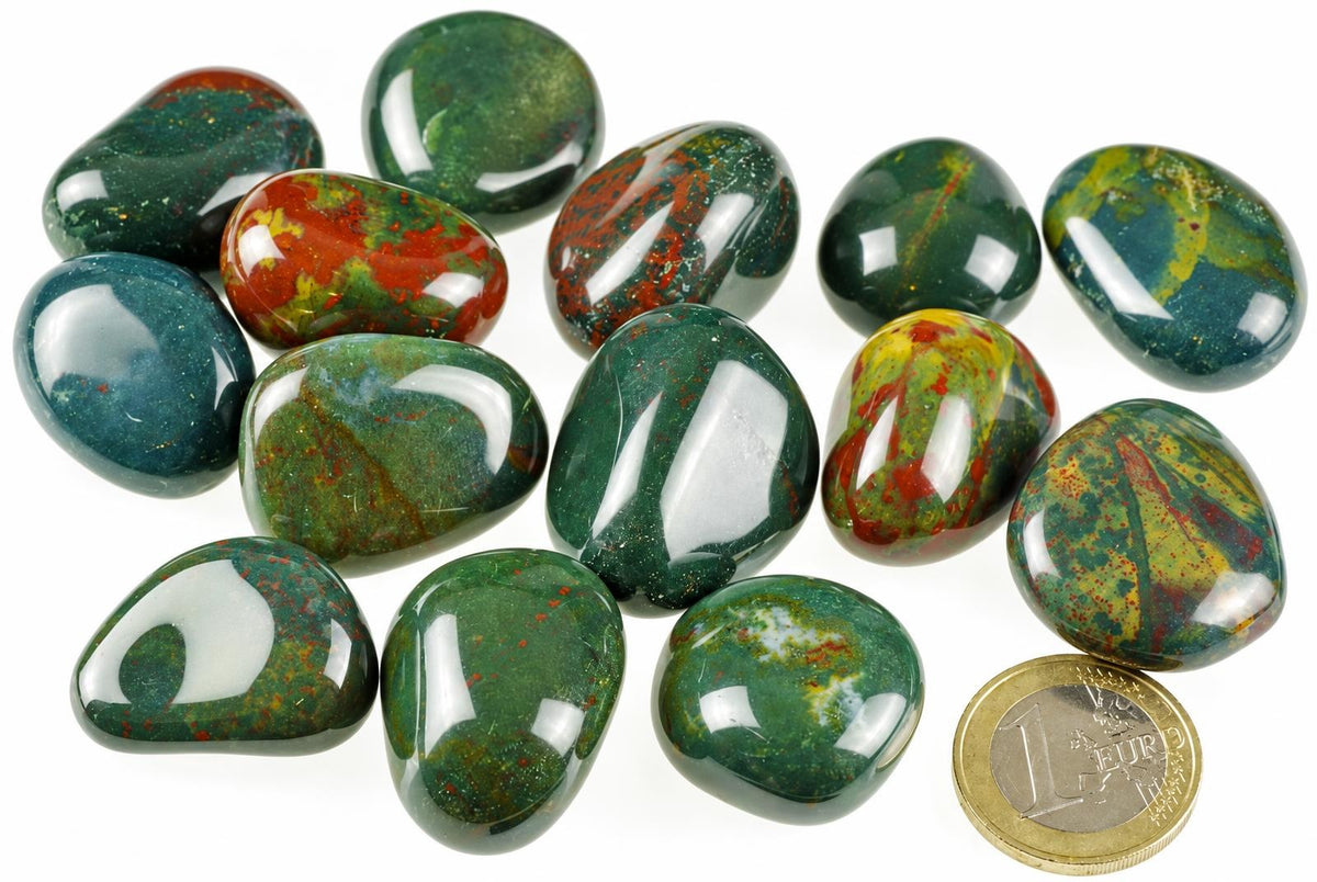 A collection of polished Heliotrope stones with green, red and yellow patterns on a white surface next to a one euro coin.