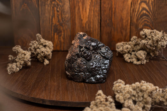 A dark, bumpy rock sits on a wooden surface with dried flowers nearby.