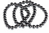 A dark, metallic bracelet made of round beads arranged in a loose coil on a white surface.