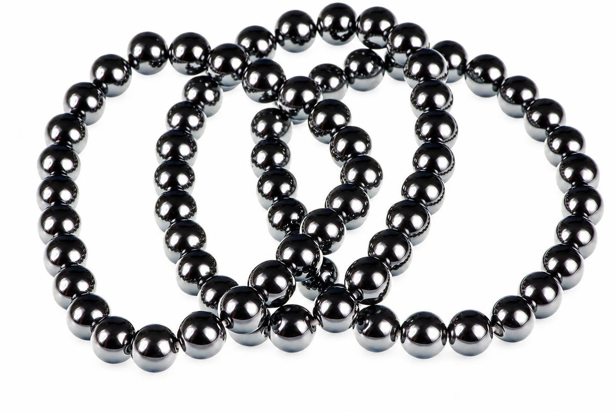 A dark, metallic bracelet made of round beads arranged in a loose coil on a white surface.