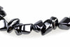 A strand of polished, irregular black beads with a metallic sheen lies on a white surface.