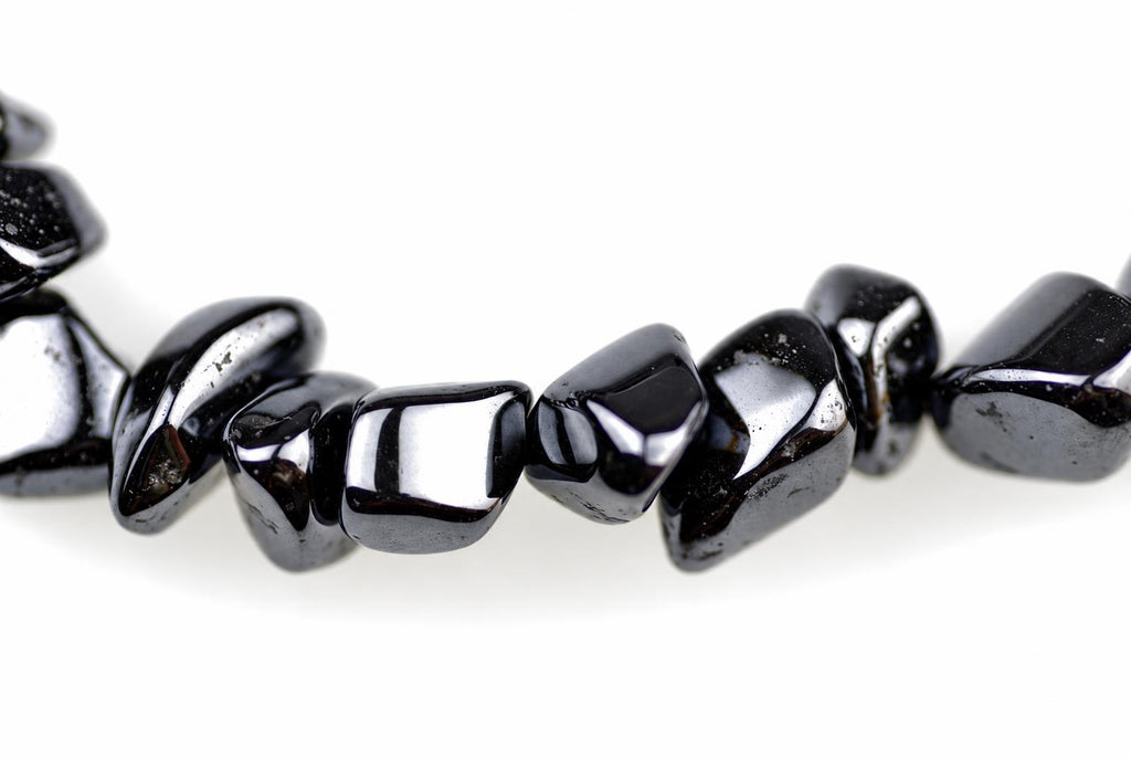 A strand of polished, irregular black beads with a metallic sheen lies on a white surface.