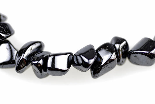 A strand of polished, irregular black beads with a metallic sheen lies on a white surface.