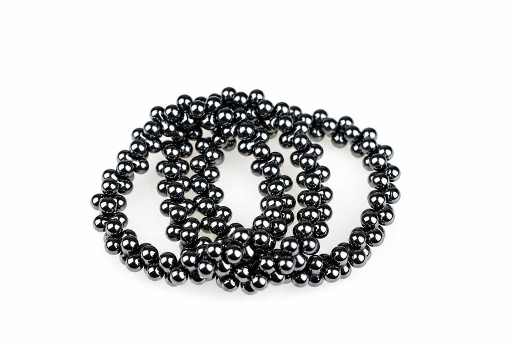 A coiled bracelet made of glossy black spherical beads on a white surface.