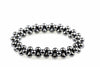 A bracelet made of dark, metallic spherical beads arranged in a circular shape on a white surface.