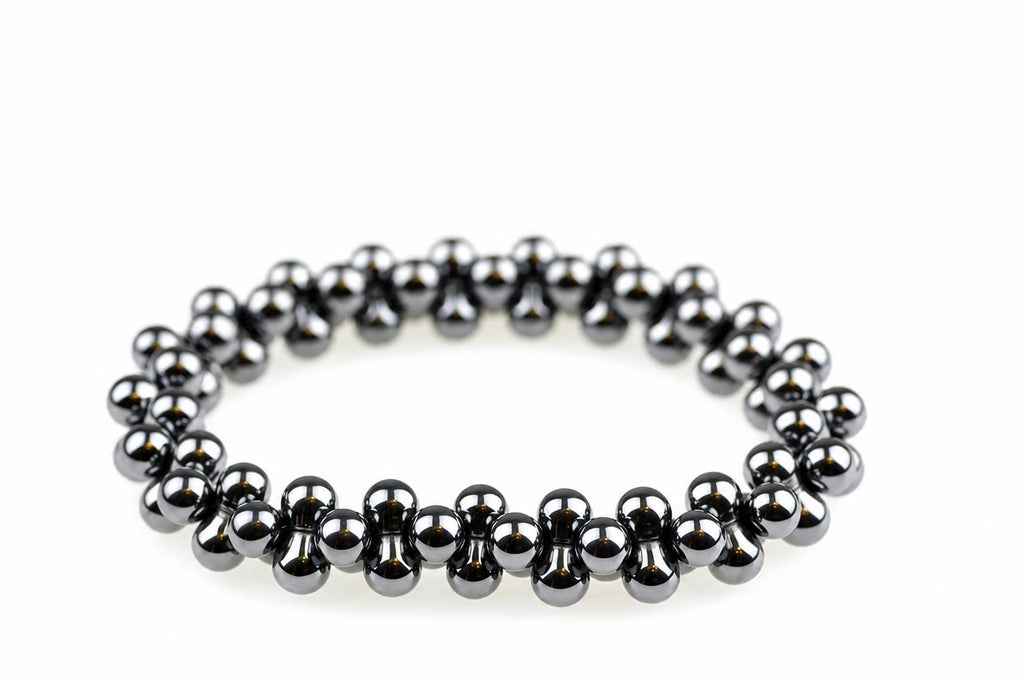 A bracelet made of dark, metallic spherical beads arranged in a circular shape on a white surface.