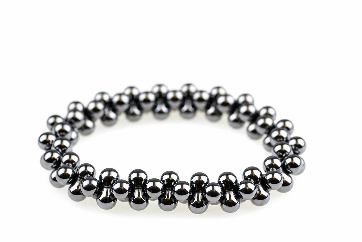 A bracelet made of dark, metallic spherical beads arranged in a circular shape on a white surface.