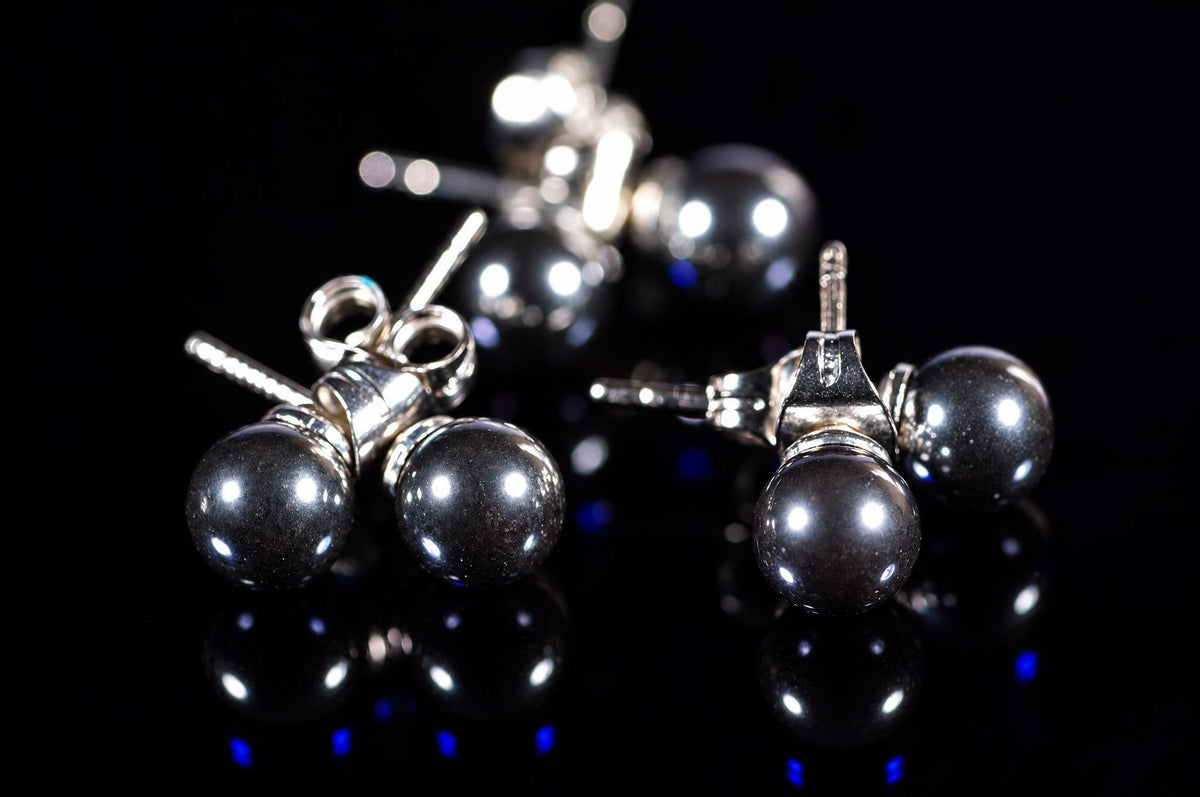 Three pairs of round, dark metallic stud earrings with silver-toned posts on a black reflective surface.