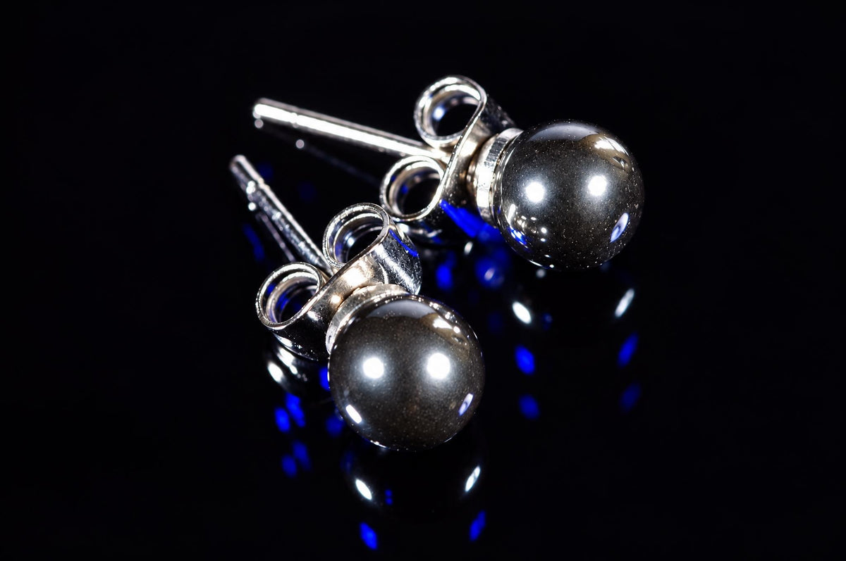 Two silver-toned stud earrings with round, dark metallic beads on a black reflective surface.