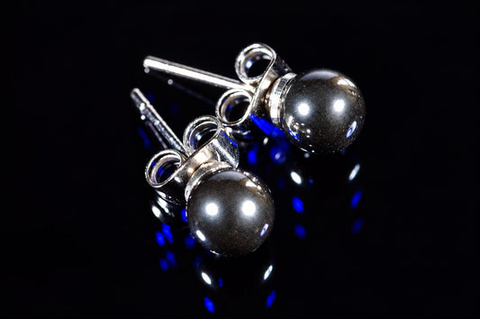 Two silver-toned stud earrings with round, dark metallic beads on a black reflective surface.