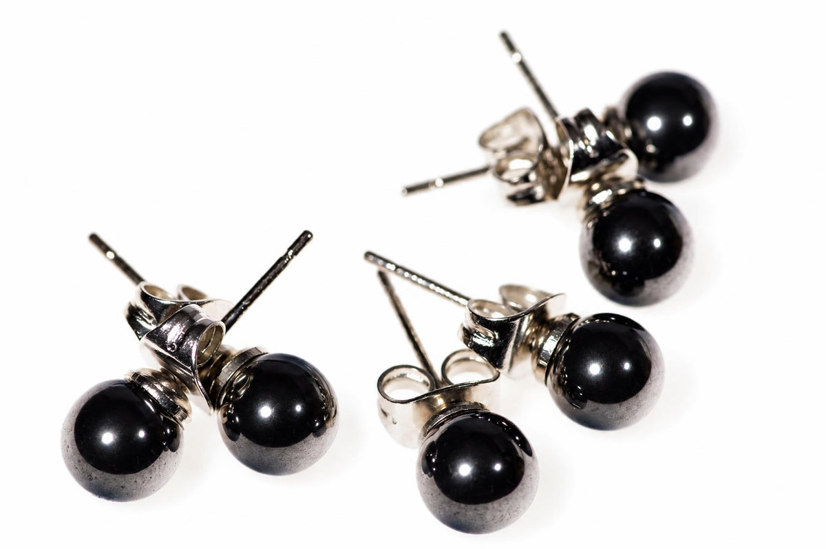 Four silver-toned stud earrings with round black beads on a white surface.