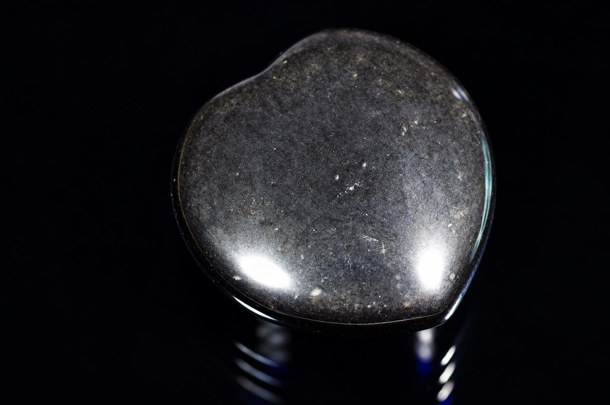 A polished, dark grey heart-shaped stone with a smooth surface and light reflections on a black background.