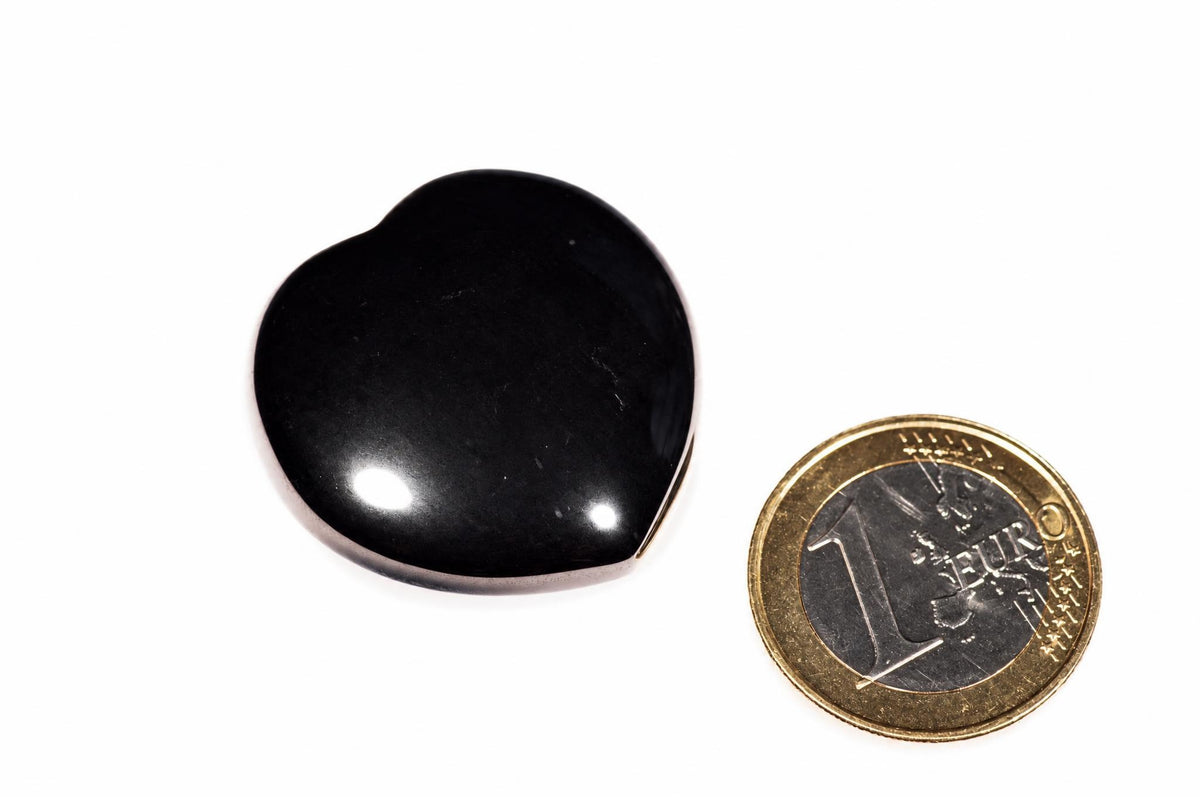 A polished, heart-shaped black stone sits on a white surface next to a one-euro coin for scale.