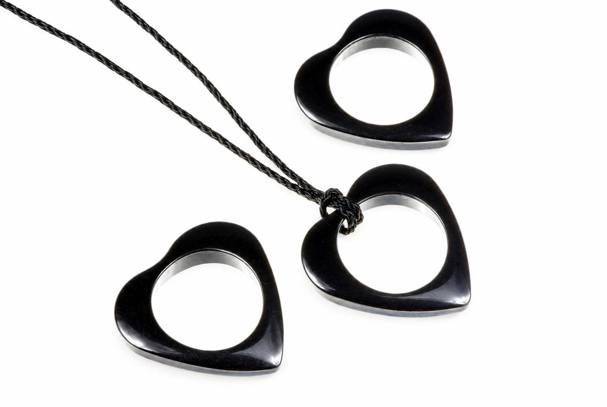 Three black heart-shaped pendants with silver-toned inner rings, one on a dark cord against a pale surface.
