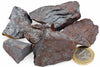 A pile of dark grey and reddish-brown raw hematite rocks on a white surface, next to a one euro coin.