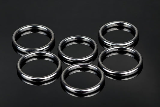 Six silver-toned rings with smooth, rounded edges arranged on a dark reflective surface.