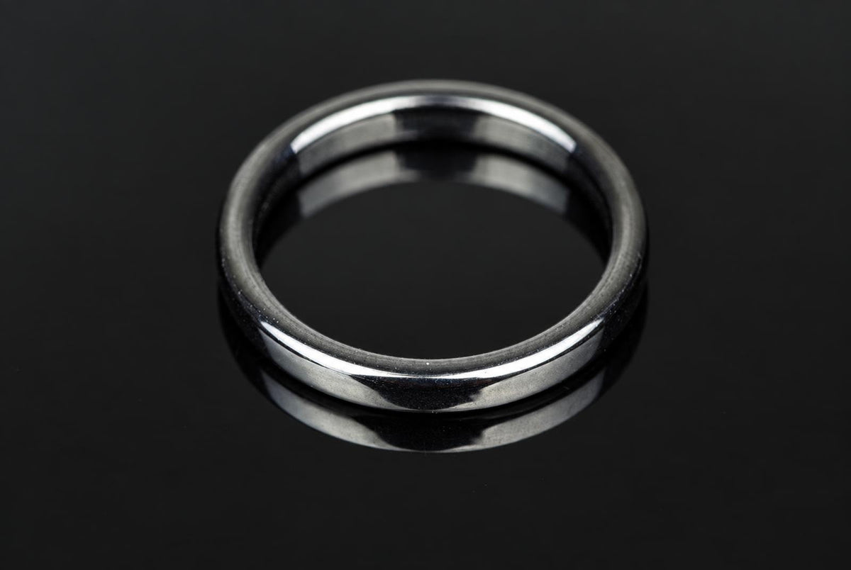 A silver-toned ring with a smooth, rounded band rests on a dark, reflective surface.