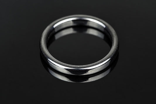 A silver-toned ring with a smooth, rounded band rests on a dark, reflective surface.