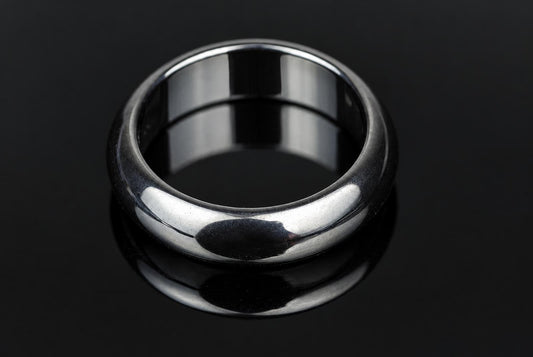 A silver-toned ring with a smooth, rounded band sits on a dark, reflective surface.
