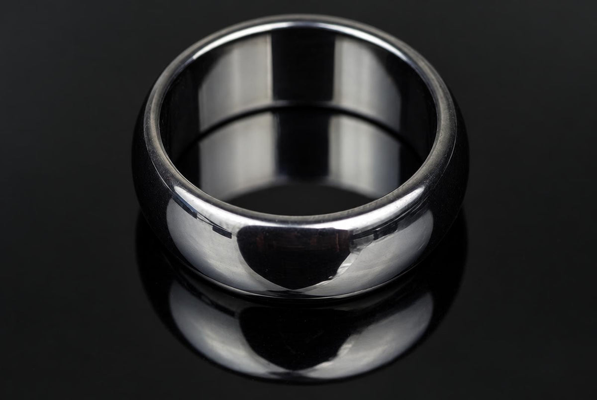A polished silver-toned ring with a smooth, rounded band sits on a dark, reflective surface.