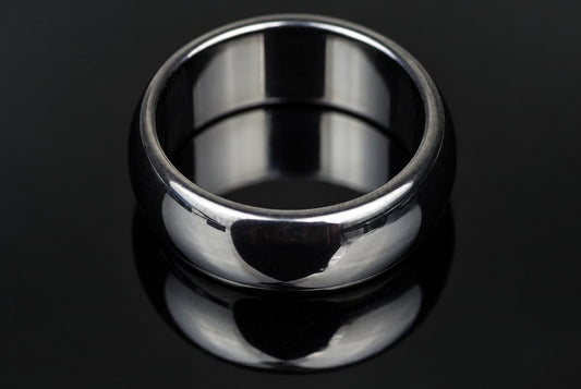 A polished silver-toned ring with a smooth, rounded band sits on a dark, reflective surface.