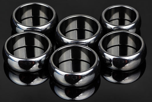 Six polished silver-toned rings arranged on a dark, reflective surface.