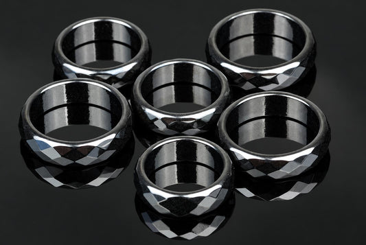 Six black faceted rings with silver-toned highlights arranged on a dark reflective surface.