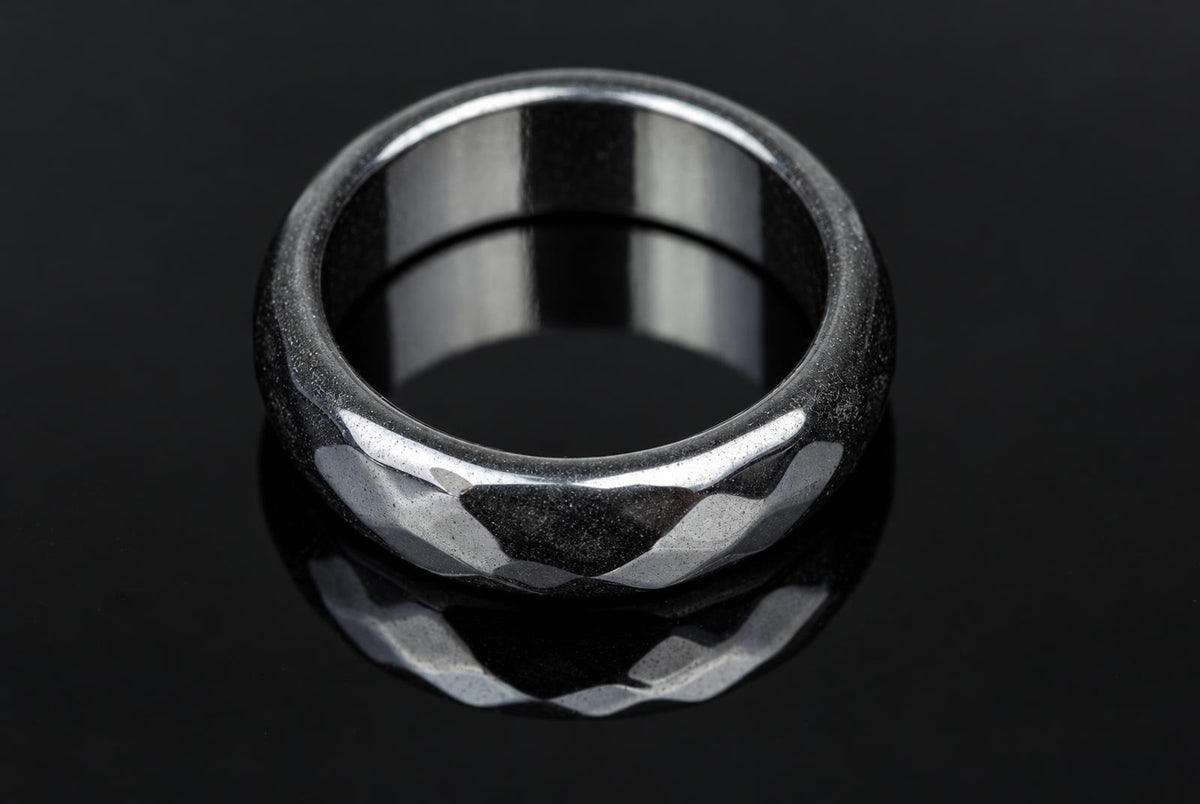 A silver-toned ring with a faceted, textured exterior and smooth interior sits on a dark reflective surface.