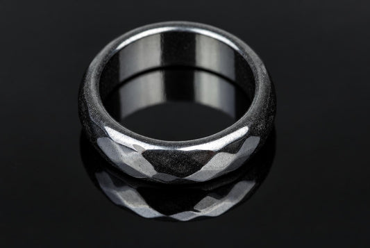 A silver-toned ring with a faceted, textured exterior and smooth interior sits on a dark reflective surface.
