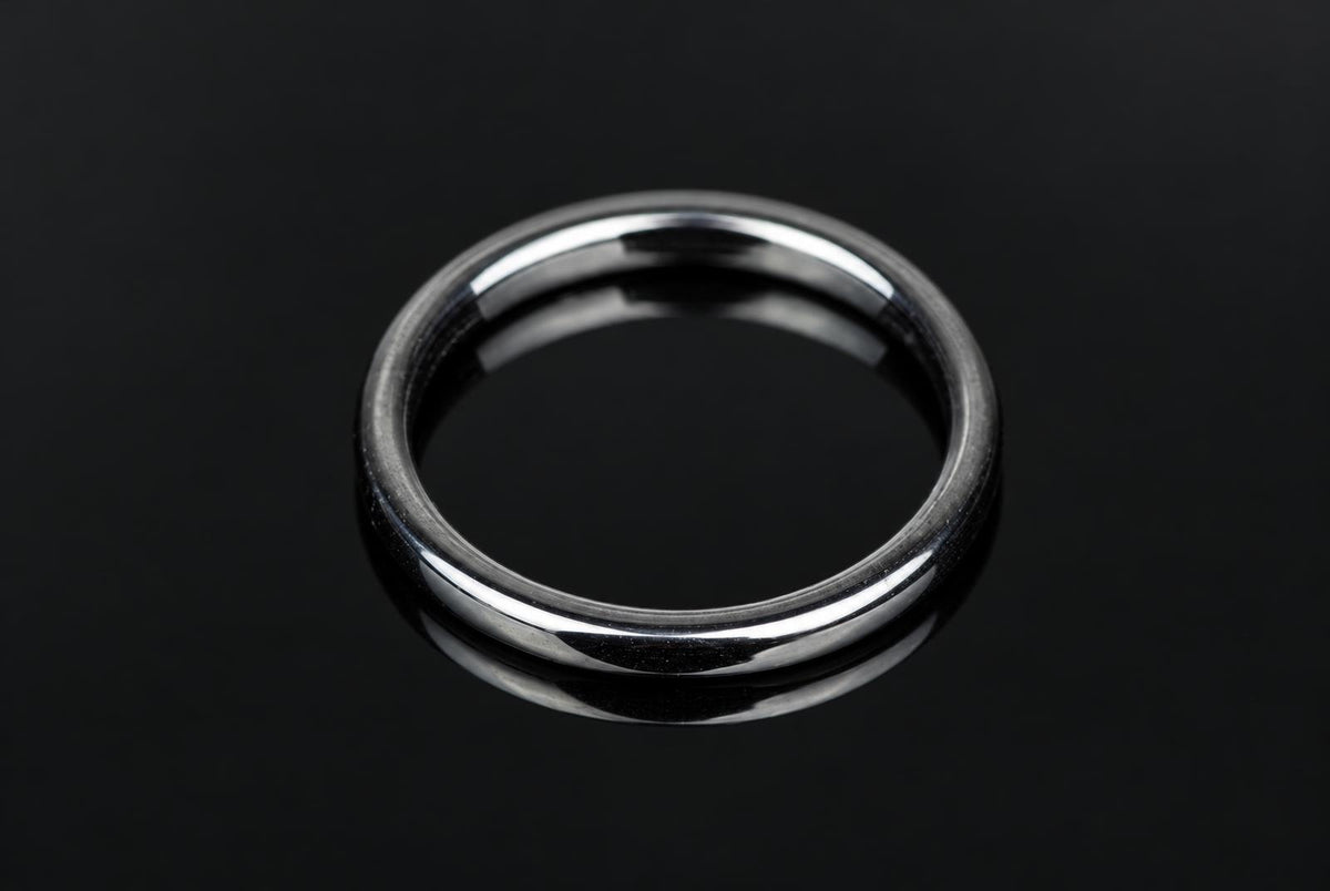 A silver-toned ring with a smooth, flat band rests on a dark, reflective surface.