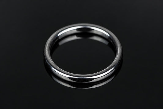 A silver-toned ring with a smooth, flat band rests on a dark, reflective surface.