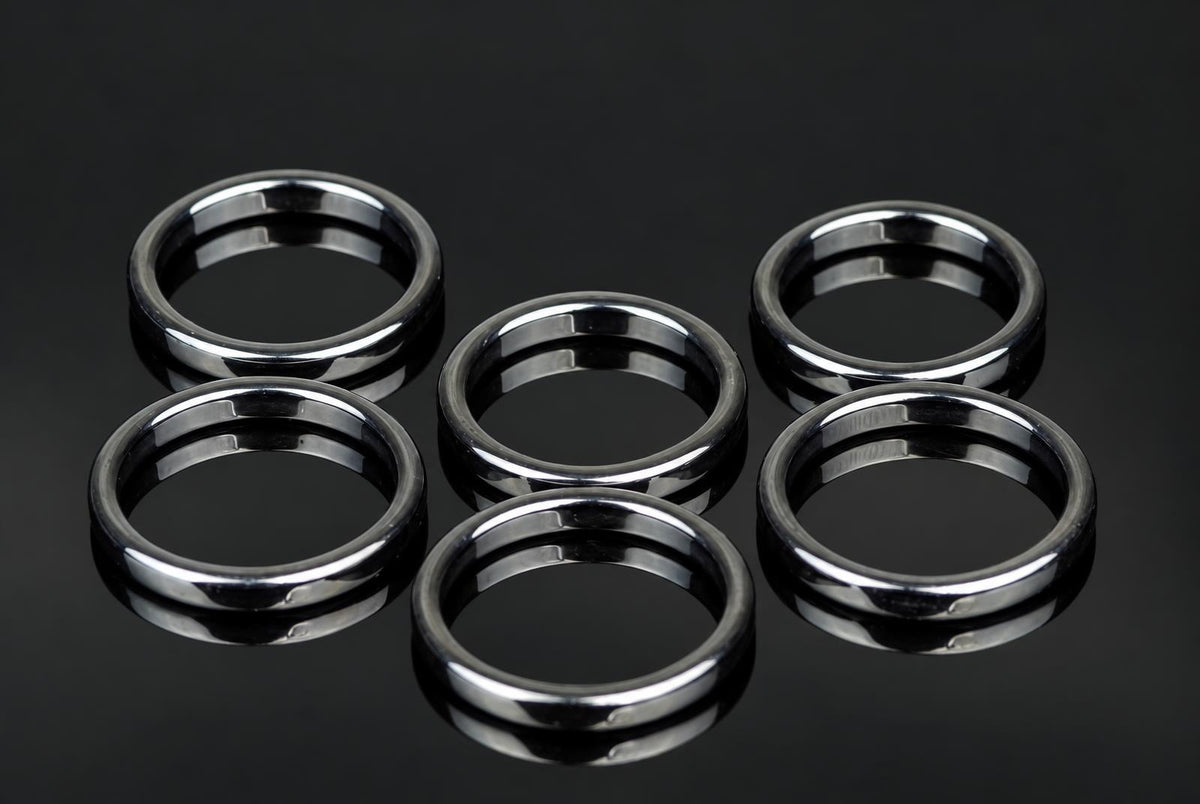 Six silver-toned rings with a smooth, flat band design arranged on a dark reflective surface.