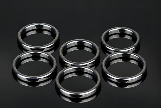 Six silver-toned rings with a smooth, flat band design arranged on a dark reflective surface.