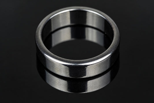 A silver-toned ring with a flat, polished band sits on a dark, reflective surface.