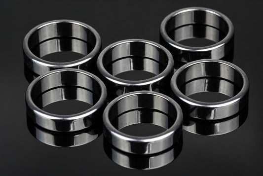 Six silver-toned rings with a smooth, flat band design arranged on a dark reflective surface.