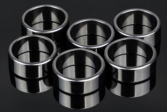 Six silver-toned, flat rings with a smooth, reflective surface arranged on a dark background.