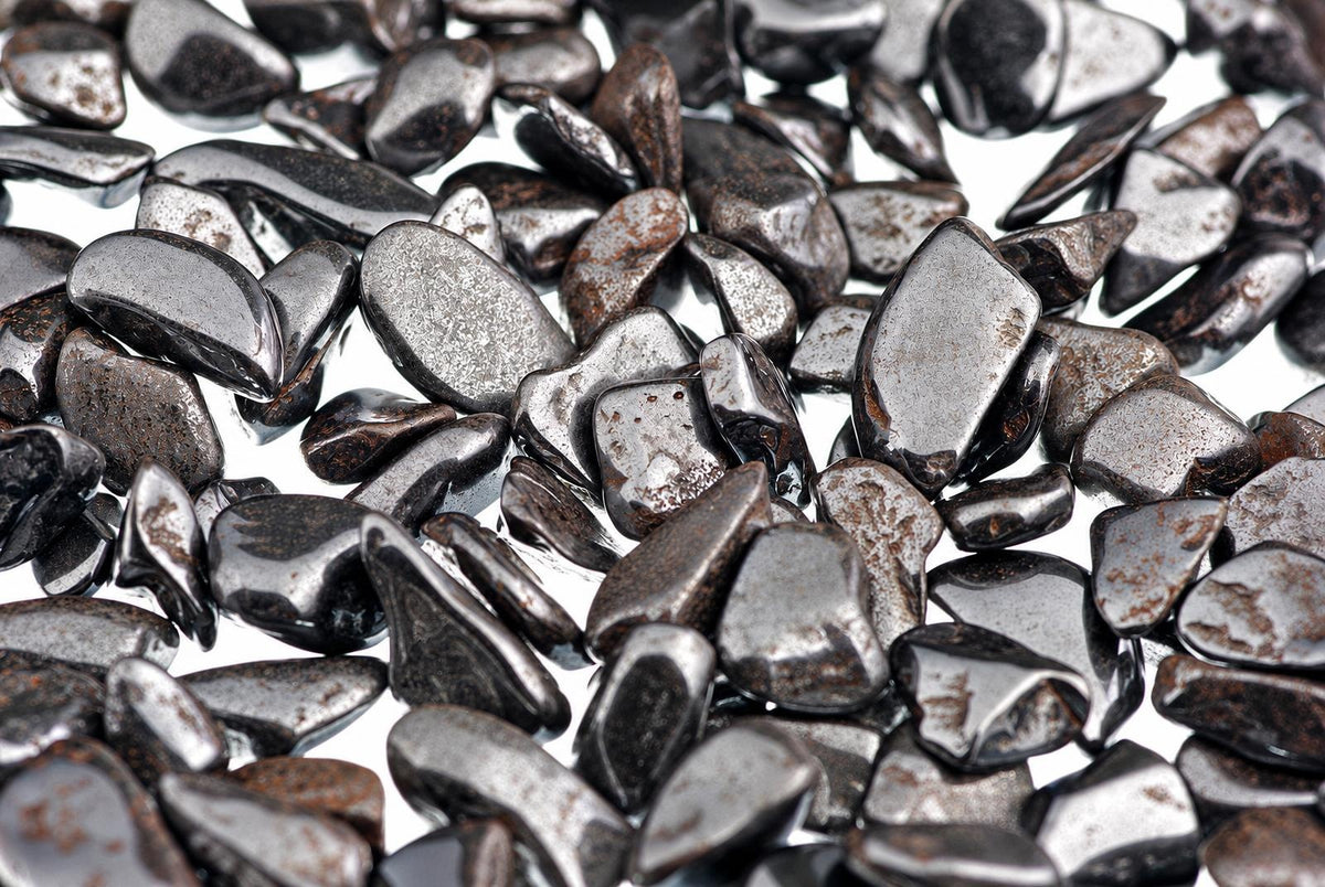 A pile of small, smooth, dark grey and black polished stones with a metallic sheen scattered on a white surface.