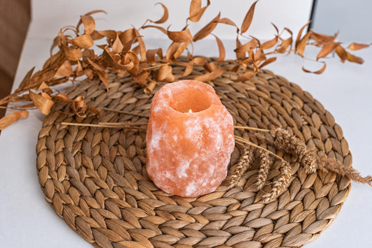 A lit Himalayan rock salt candle sits on a woven brown mat, surrounded by dried leaves and wheat stalks.